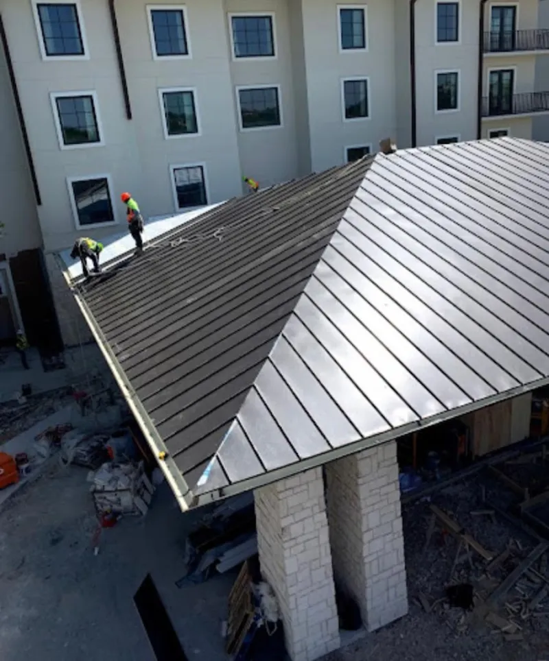 Crew installing standing seam metal roof panels on a commercial project in Lavon